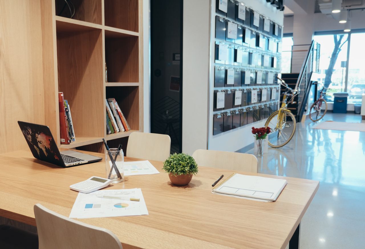 heros-img A modern office workspace featuring a laptop, documents, and a potted plant on a wooden table.