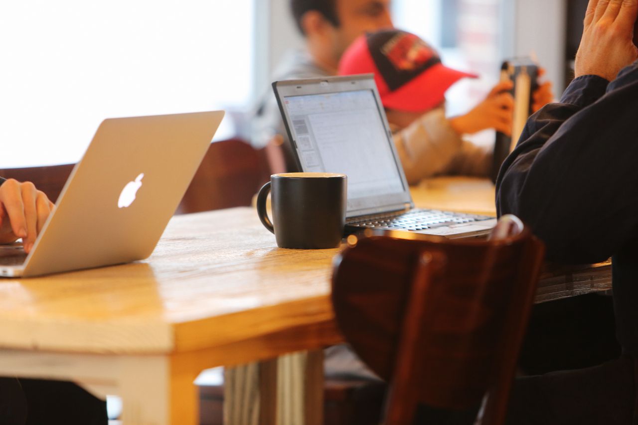 our-story Group working in a cozy cafe with laptops and coffee mugs on a shared table.